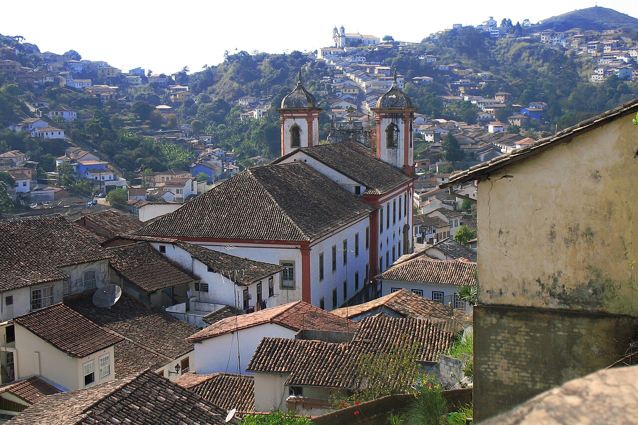 Matriz de Antônio Dias com suas duas torres entre telhados coloniais e morros