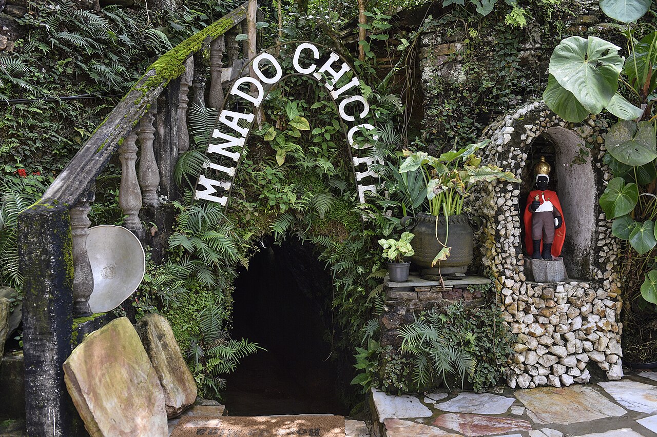 Entrada da Mina do Chico Rei cercada de plantas, com o nome escrito em arco